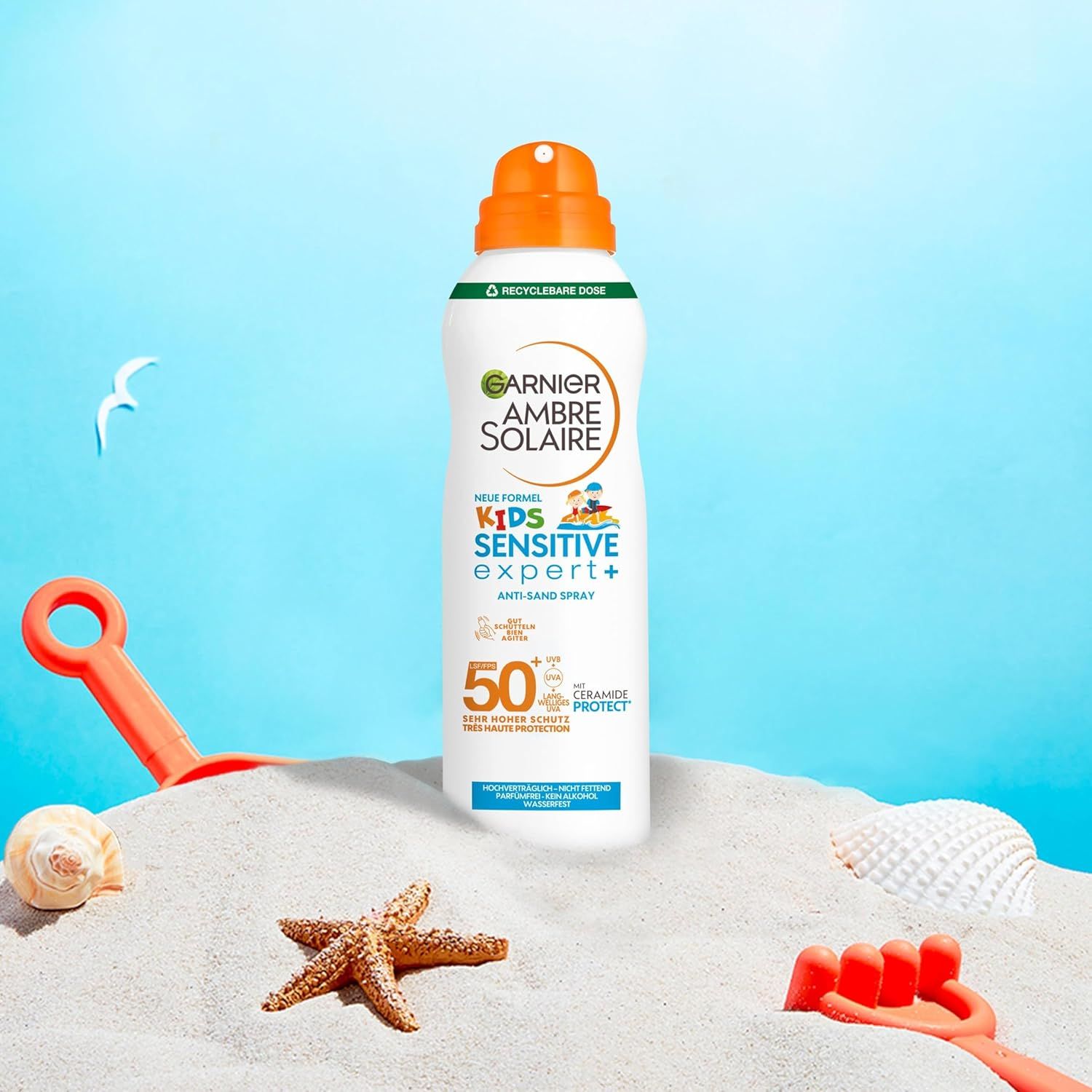 Sprayflasche auf Sand, mit Strandutensilien. Produkt: Garnier Ambre Solaire Kids Sensitive Expert+ Anti-Sand Spray LSF 50+.
