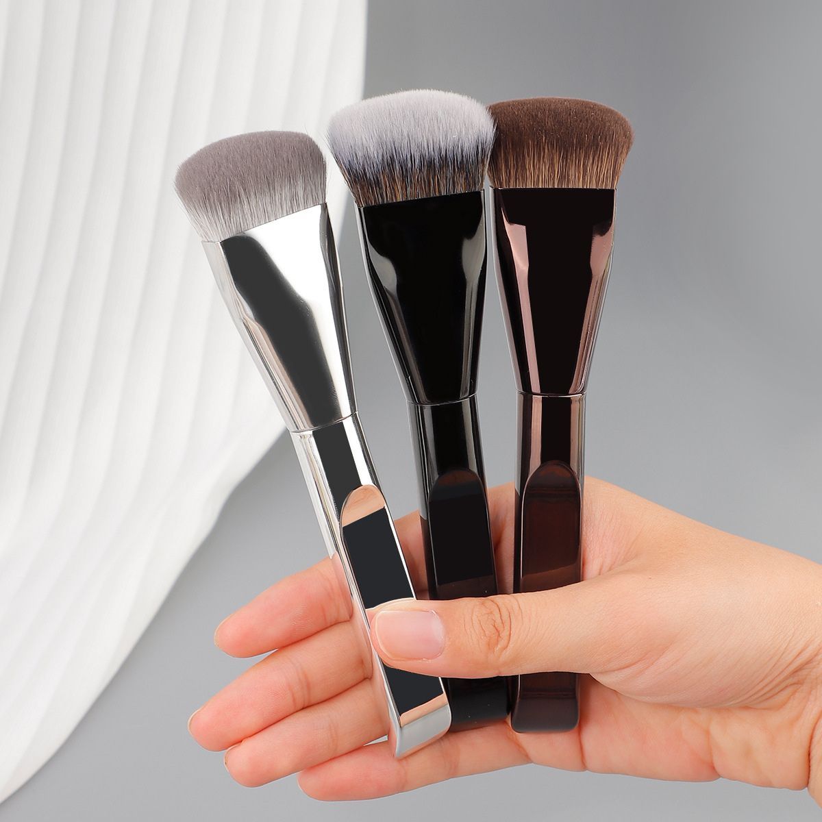 Drei flache Make-up-Pinsel mit silbernem, schwarzem und braunem Griff.