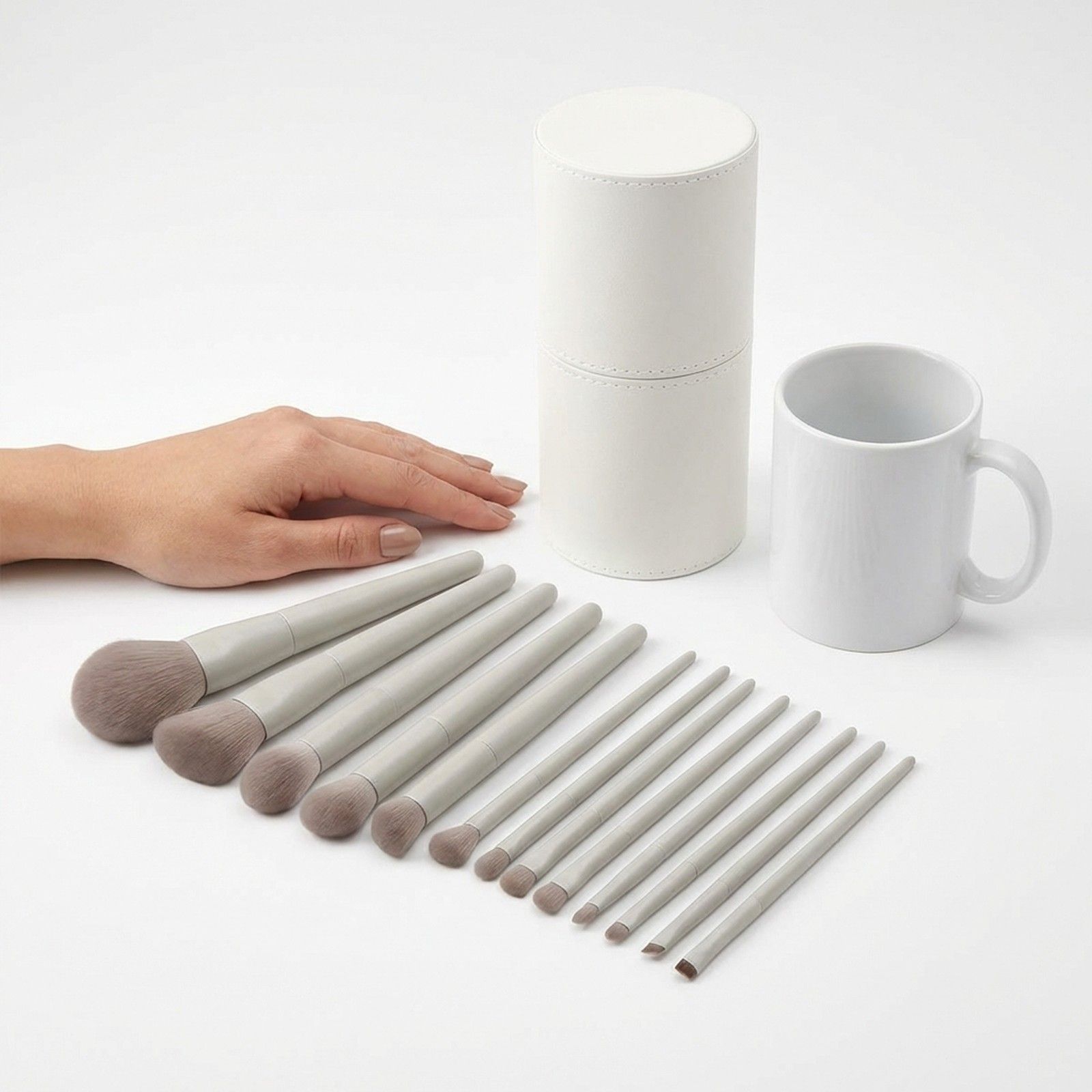 Ein Set von 12 hellgrauen Make-up-Pinseln mit weißem Griff und einer runden weißen Aufbewahrungsbox.