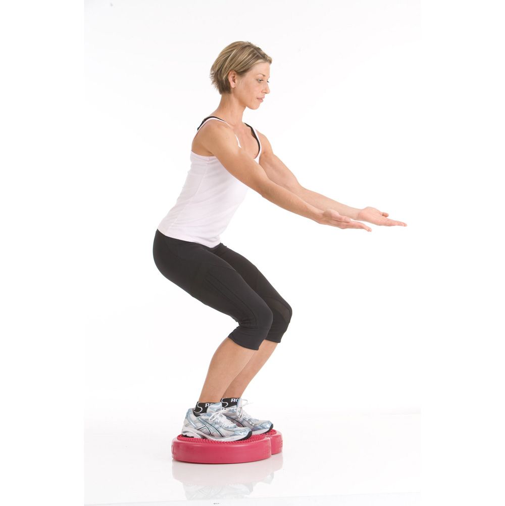 Frau macht Kniebeugen auf rotem TOGU Aero Step XL®. Sie steht auf weißem Hintergrund.