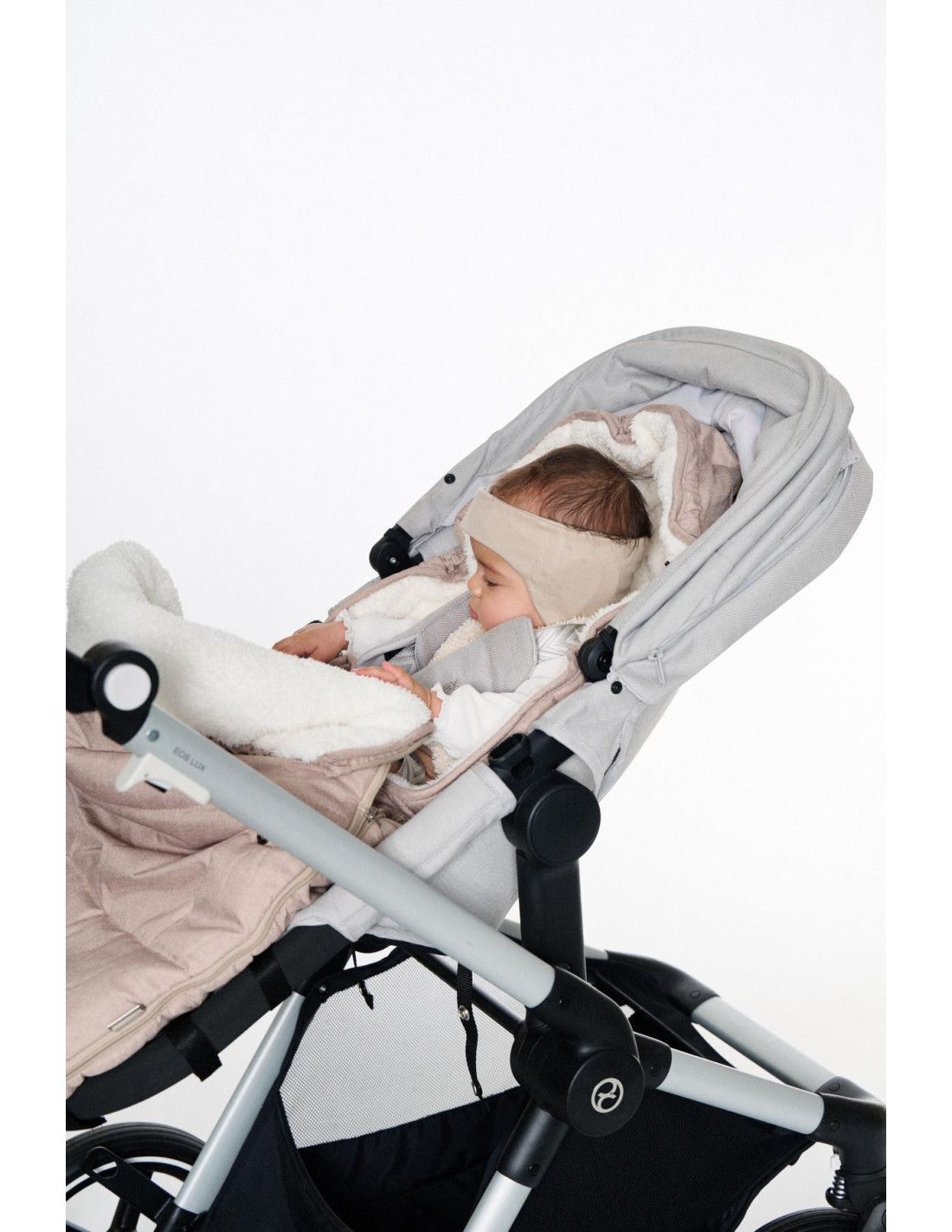 Baby in Kinderwagen mit beiger Kopfbedeckung.