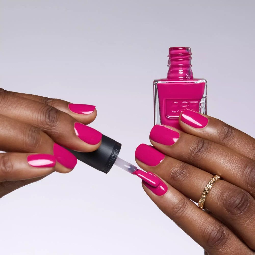 Hände lackieren Nägel mit rosa Nagellack. Flasche und Pinsel sichtbar. Ring am Finger.