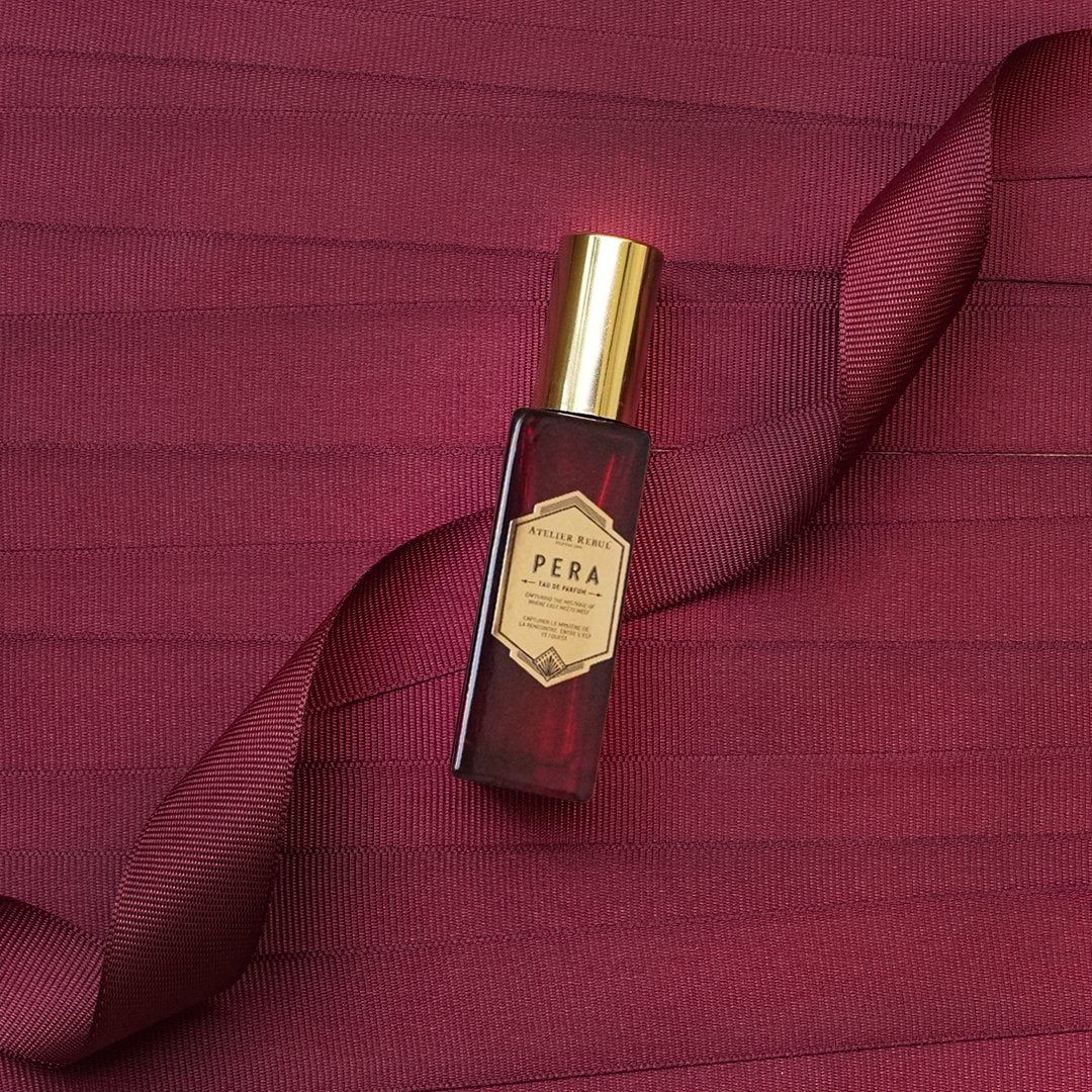 Rotes Parfümfläschchen mit goldfarbenem Verschluss und Etikett. Auf rotem Hintergrund mit Schleife.