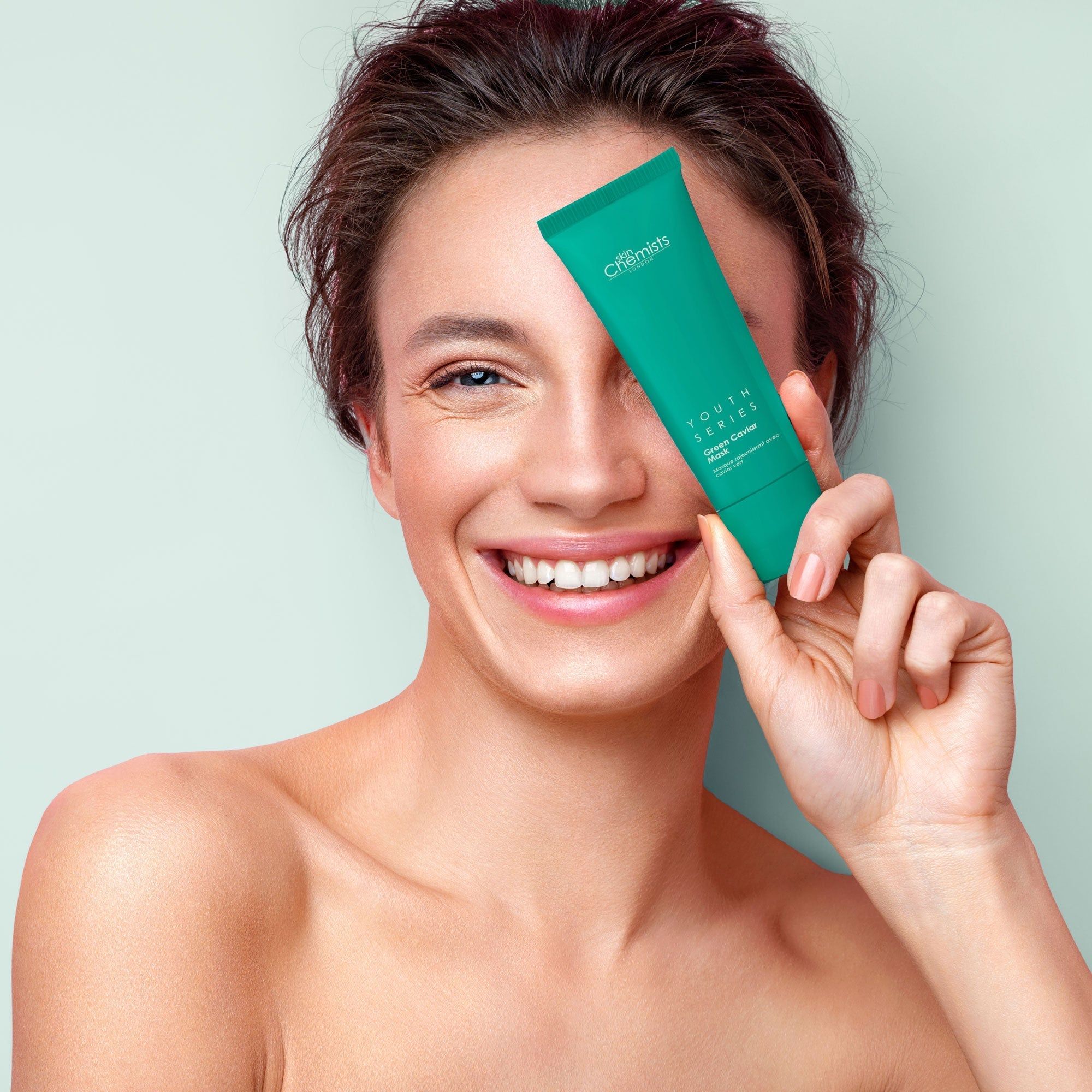 Frau hält grüne Tube vor dem Auge. Aufschrift "skinChemists" und "Youth Series".