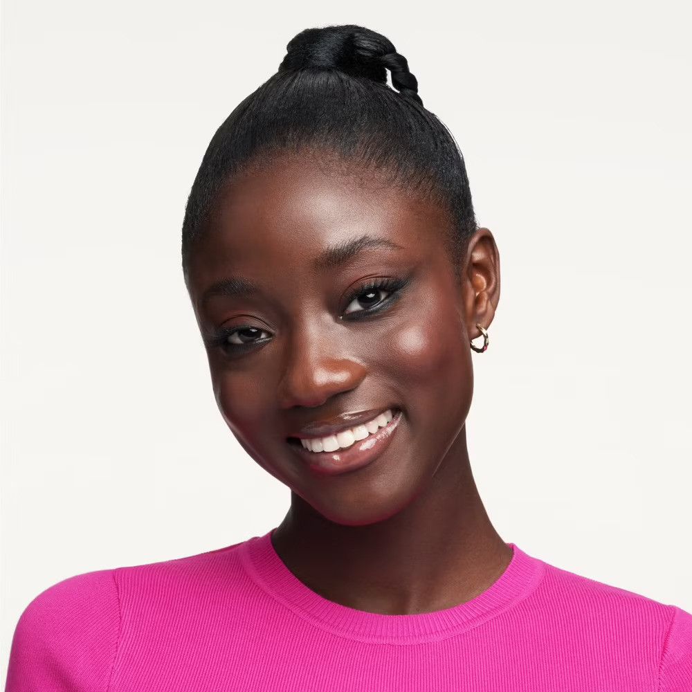 Porträt einer lächelnden Frau mit dunkler Haut. Sie trägt ein pinkfarbenes Oberteil und Ohrringe. Ihr Haar ist hochgesteckt.