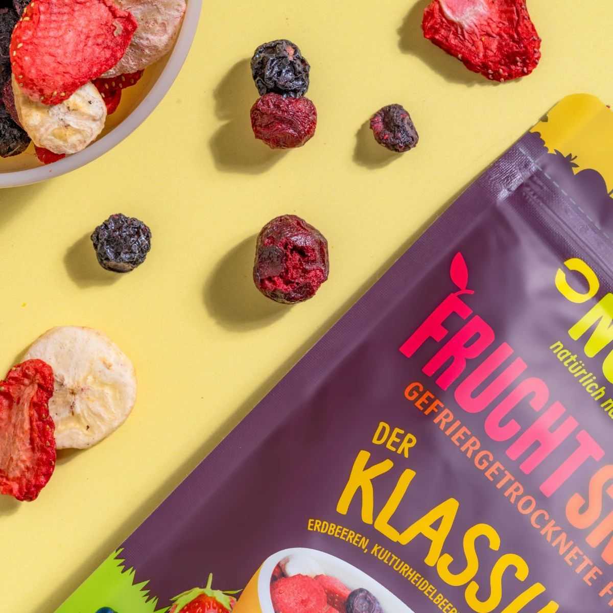 Nahaufnahme von gefriergetrockneten Früchten. Daneben Beutel mit Aufschrift: NutriPur, Frucht Snacks, Der Klassiker.