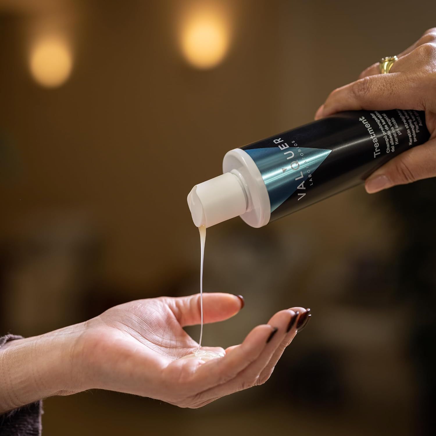 Eine Hand hält eine schwarze Flasche Valquer Treatment und gießt eine weiße Flüssigkeit in die andere Hand.