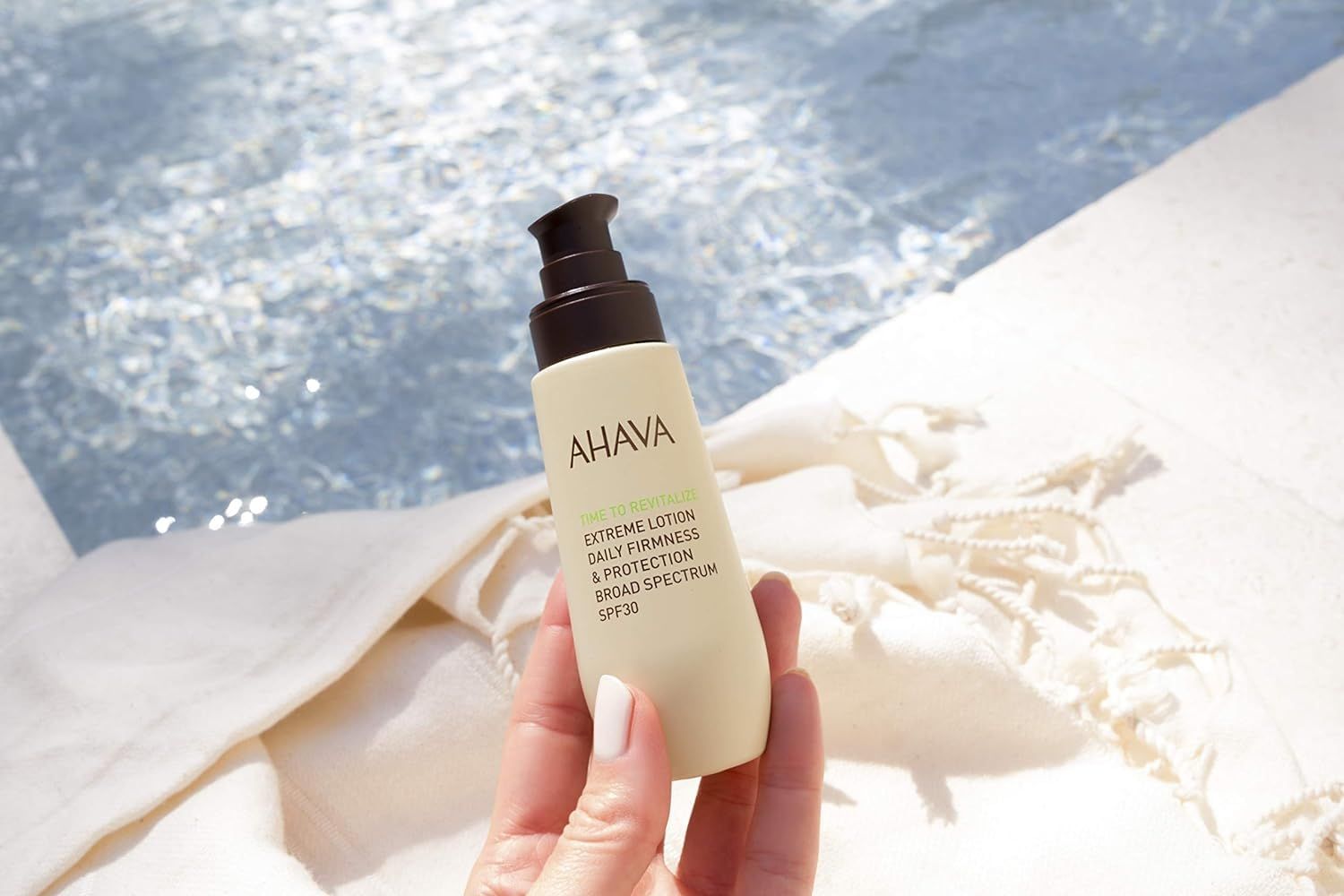 Ahava T.T.R. Extreme Lotion SPF30 wird in einer Hand neben einem Pool gehalten.