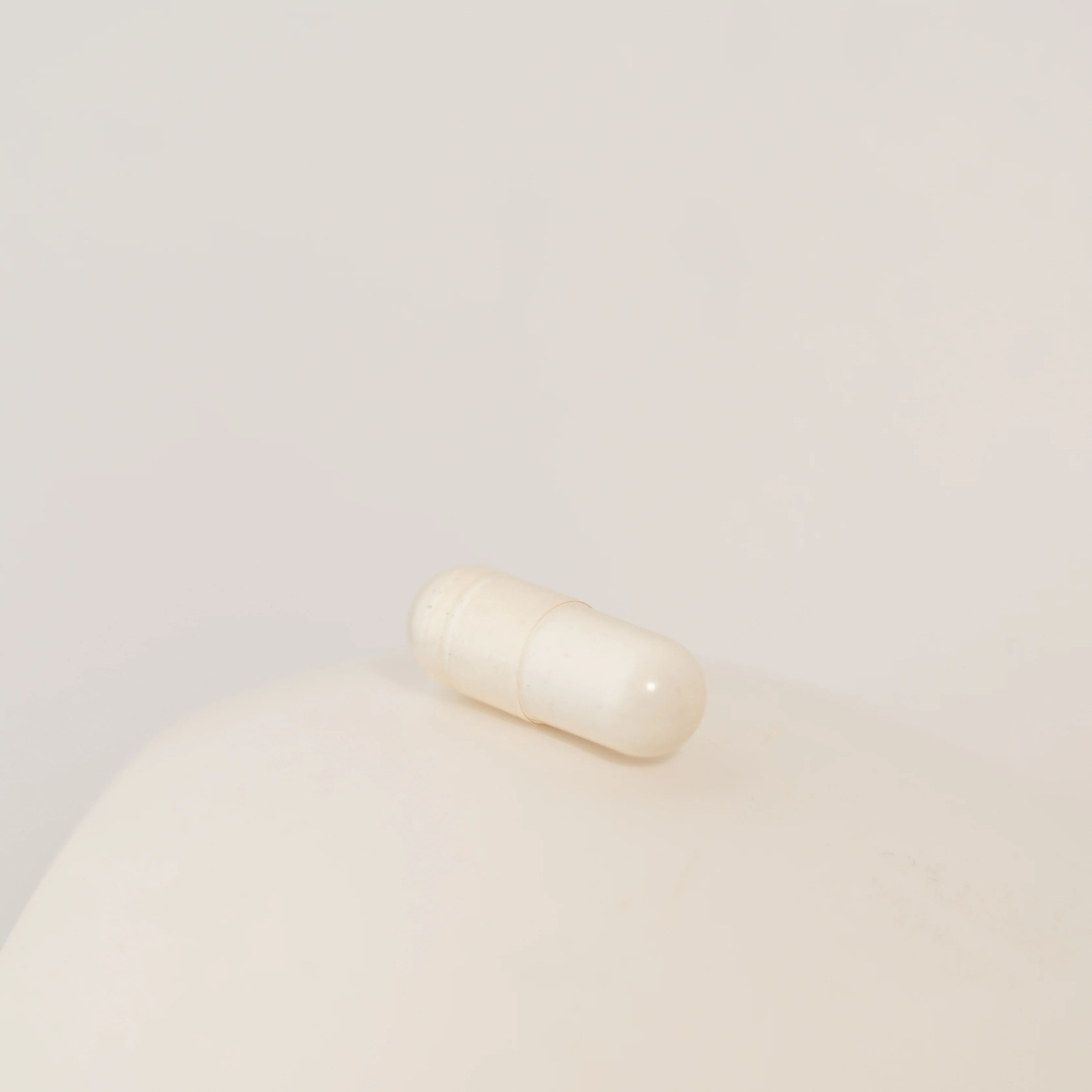 Eine einzelne, cremefarbene Kapsel. Sie liegt auf einer hellen, abgerundeten Oberfläche.