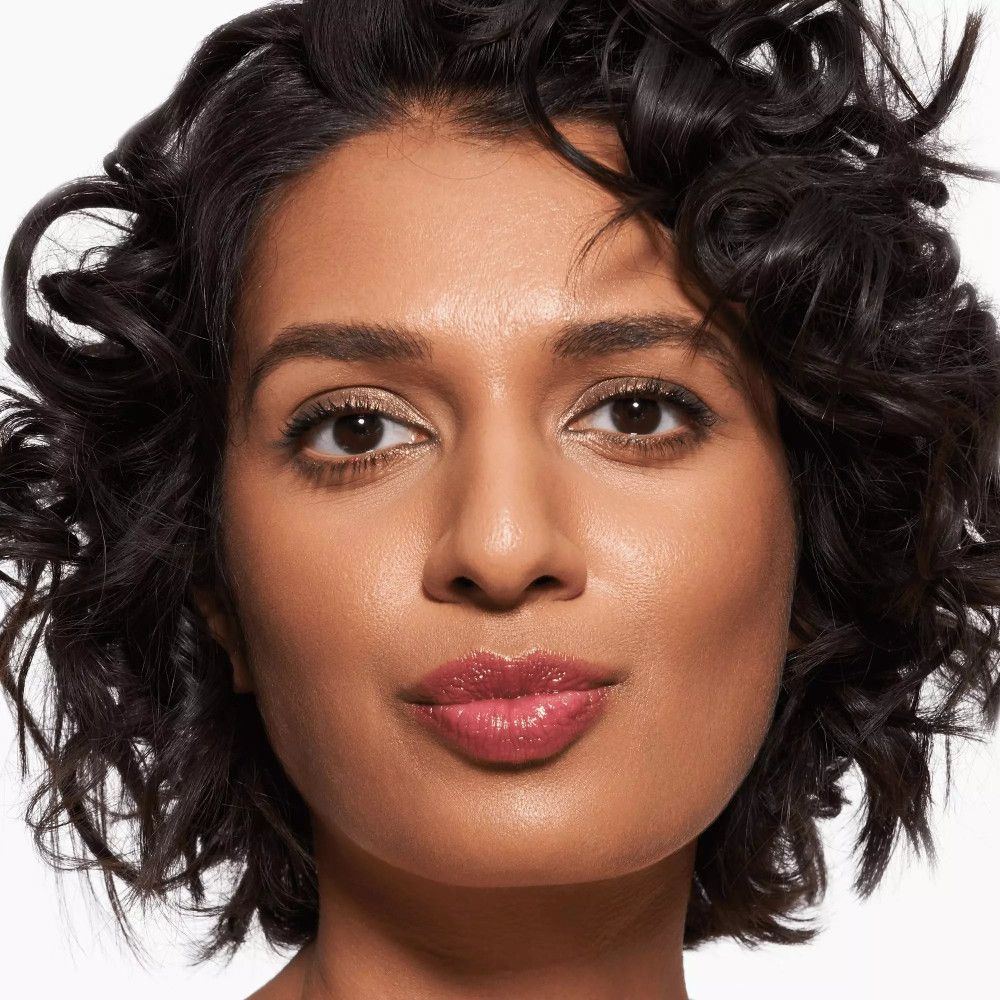 Porträt einer Frau mit rosafarbenen Lippen. Sie hat dunkle Haare und trägt Make-up.