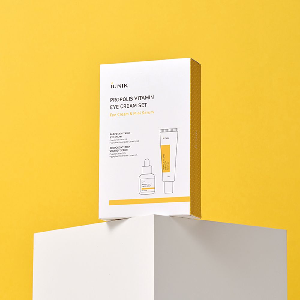 IUNIK Propolis Vitamin Eye Cream Set. Weiße Verpackung mit gelben Akzenten. Auf weißem Podest vor gelbem Hintergrund. Text sichtbar.