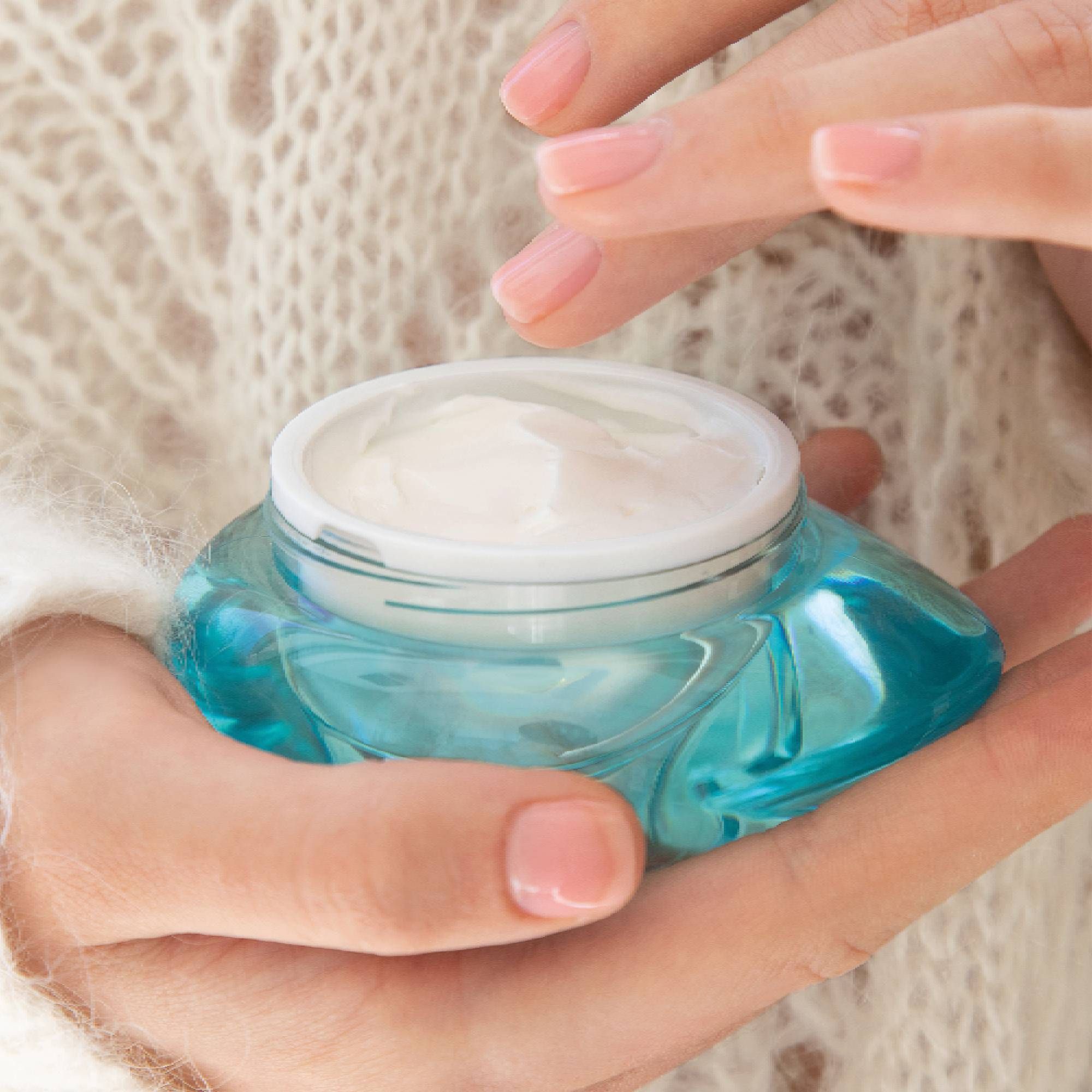 Offener, türkisfarbener Tiegel mit Creme. Hände halten den Tiegel. Marke THALGO.