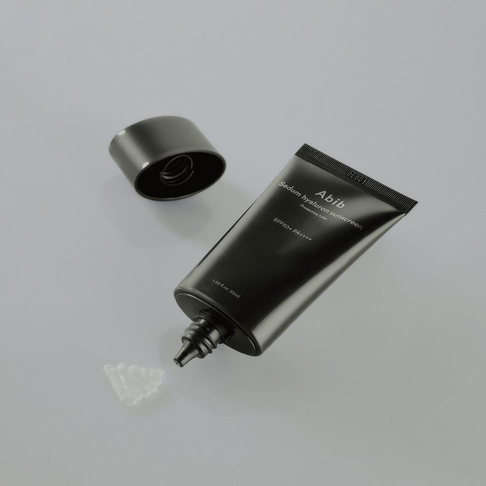 Schwarze Tube, Kappe daneben. Produkt wird aus der Tube gedrückt. Produktname und SPF-Angaben sind sichtbar.