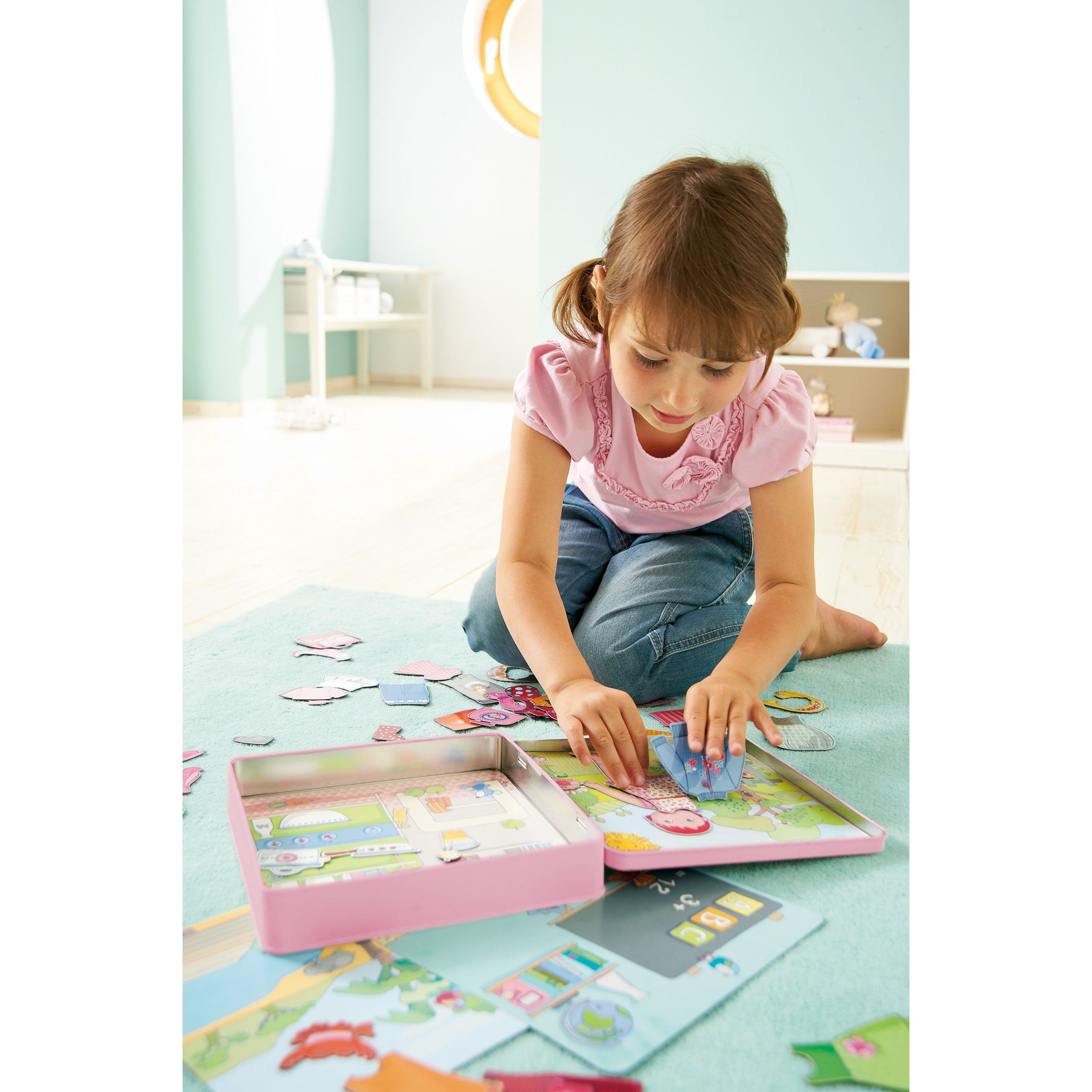Mädchen spielt mit Anziehpuppe Lilli. Rosa Metallbox mit magnetischen Kleidern und Kulissen. Auf blauem Teppich, im Kinderzimmer.