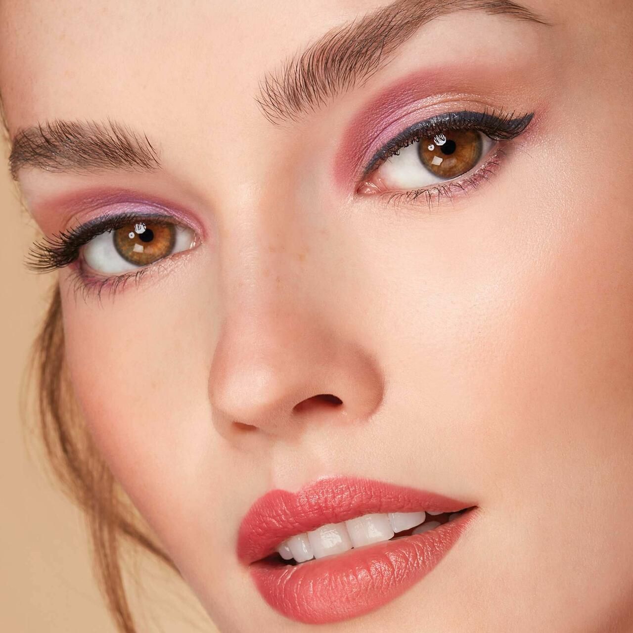 Nahaufnahme eines Gesichts mit pinkfarbenem Eyeshadow. Die Augen sind mit Eyeliner betont, die Lippen rot geschminkt.