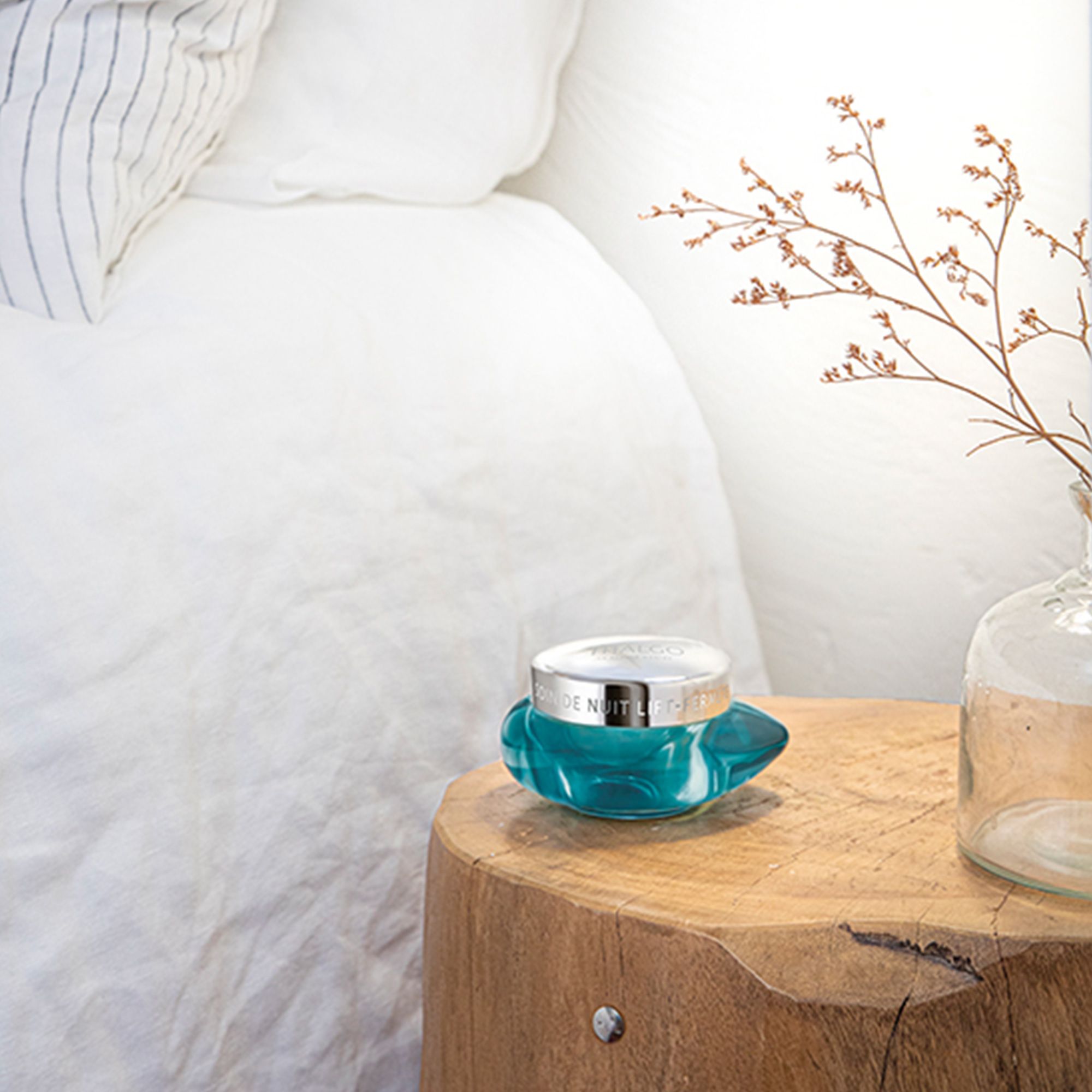 Türkisfarbener Tiegel mit silbernem Deckel auf einem Holztisch. Im Hintergrund ein Bett.