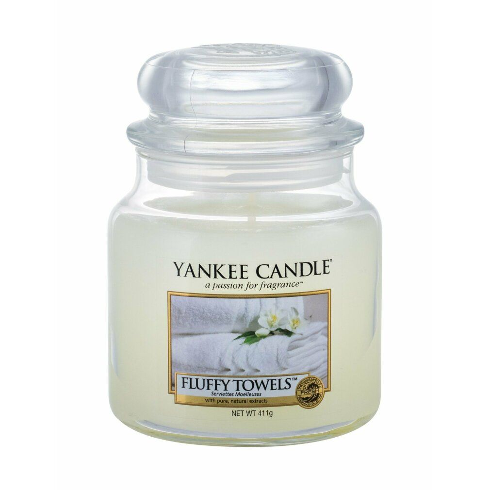 Glasbehälter mit weißem Wachs und Deckel. Etikett mit Text und Bild von Handtüchern und Blumen. "Fluffy Towels" und "Yankee Candle".
