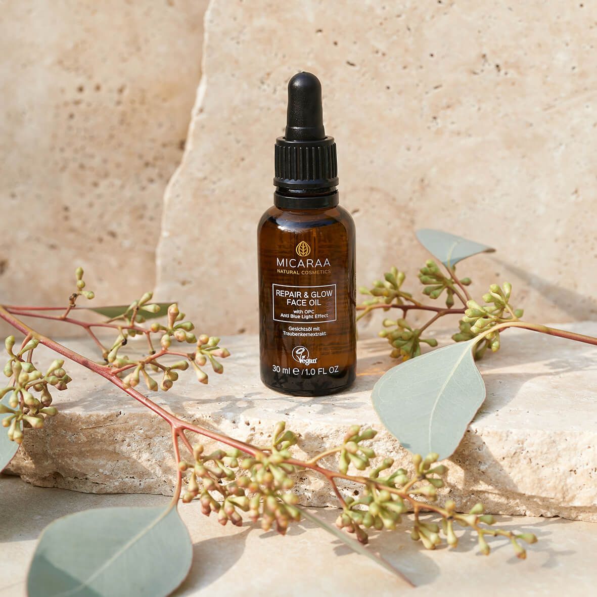 Braune Glasflasche mit Tropfer. Aufschrift: MICARAA Repair & Glow Face Oil. Vegan-Siegel. Dekoration: Zweige mit Blättern.