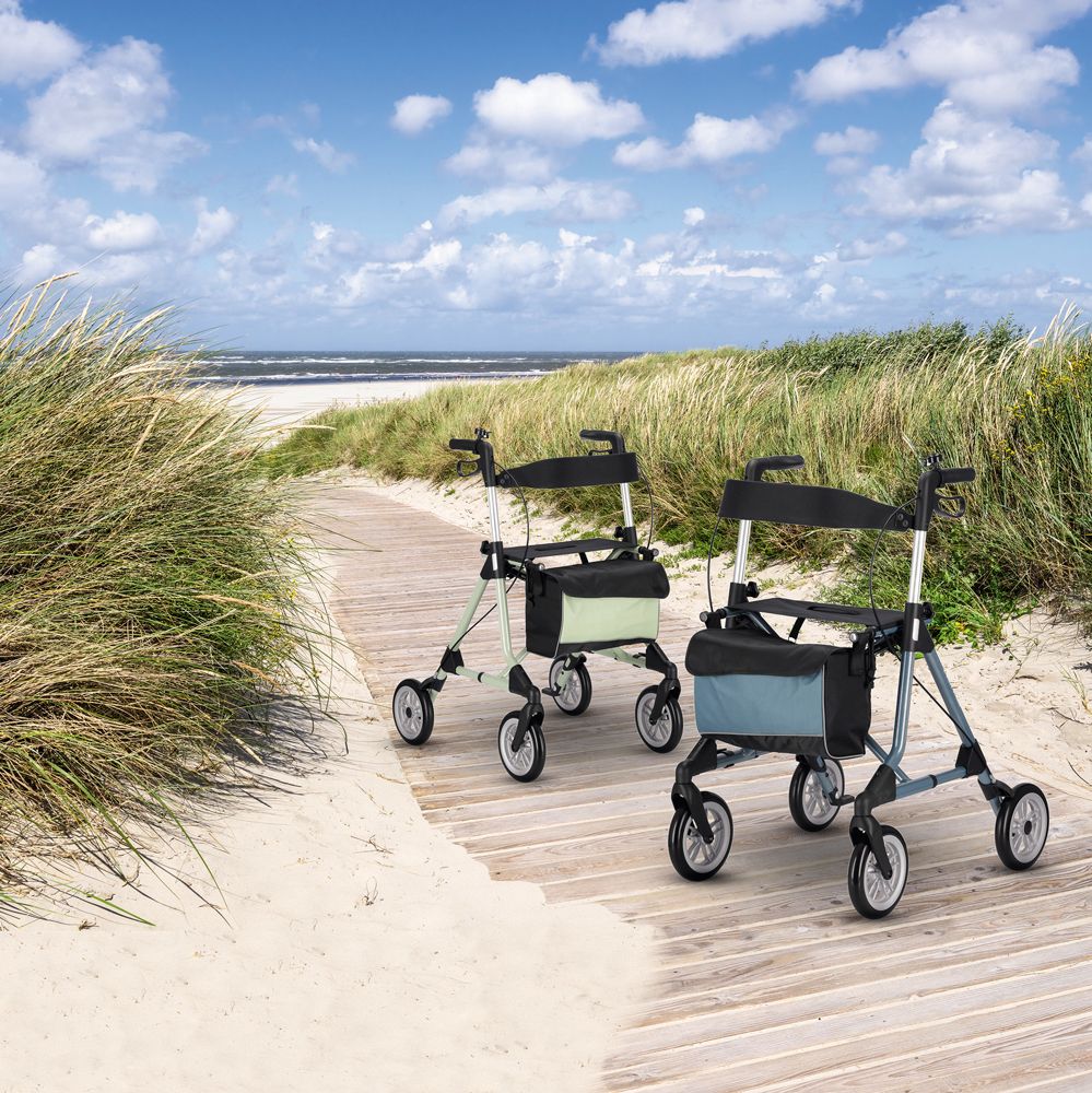 Zwei Rollatoren auf Holzsteg am Strand. Hellgrüne und blaue Rahmen, schwarze Sitze und Taschen.