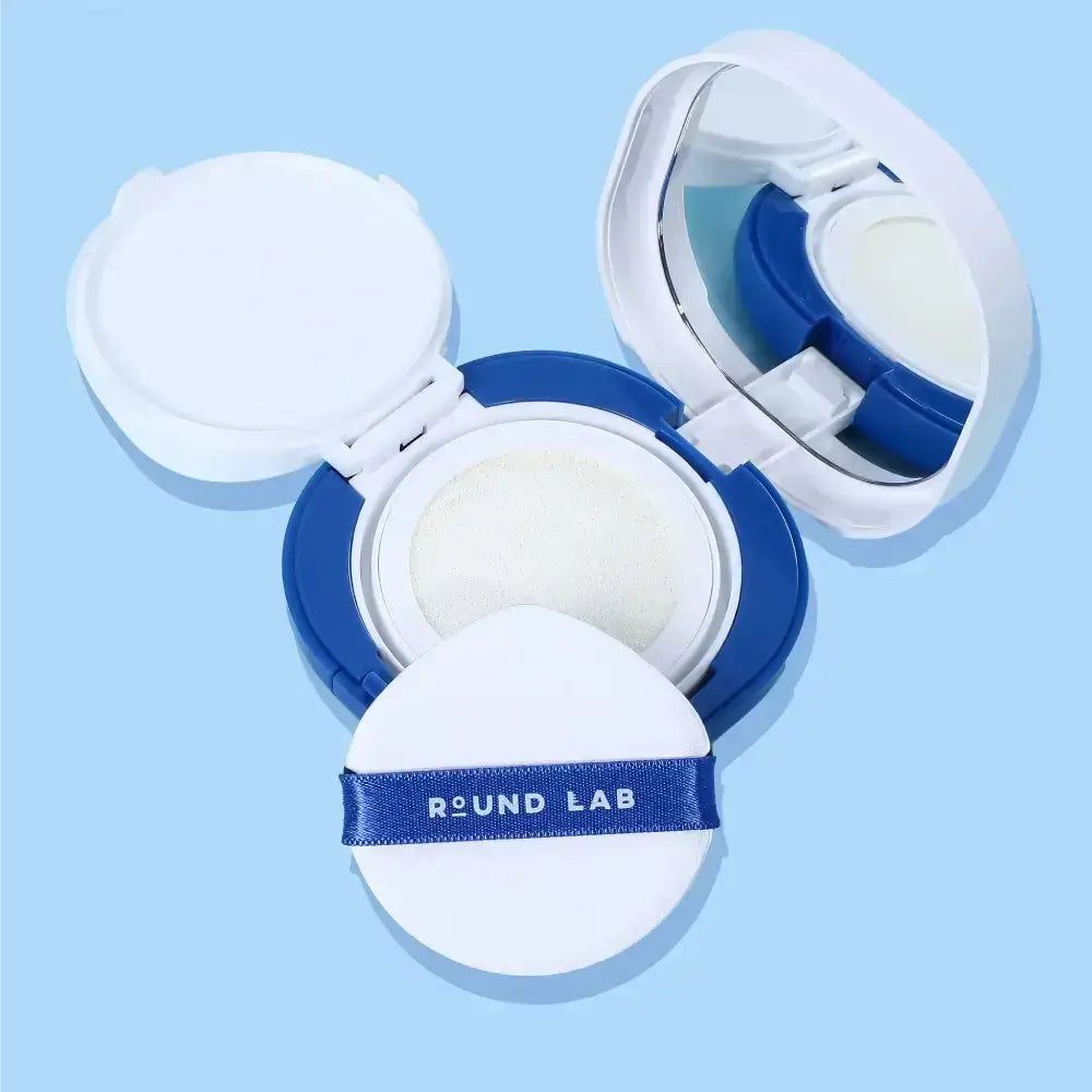 Blau-weiße Kosmetikdose mit Spiegel und Schwamm. Schwamm mit blauem Band und Schriftzug ROUND LAB. Geöffnet.