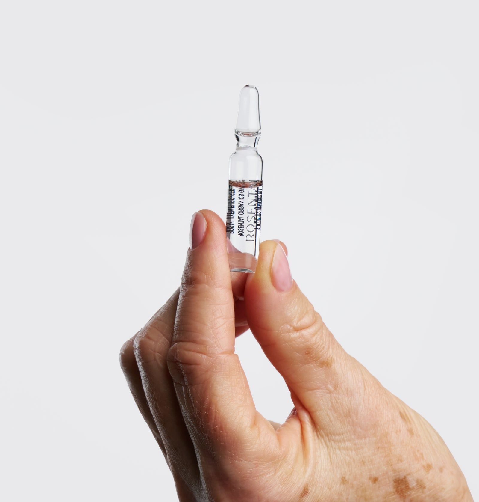 Hand hält Ampulle. Klare Flüssigkeit, Beschriftung. Glasampulle mit spitzem Ende. Helle Haut.