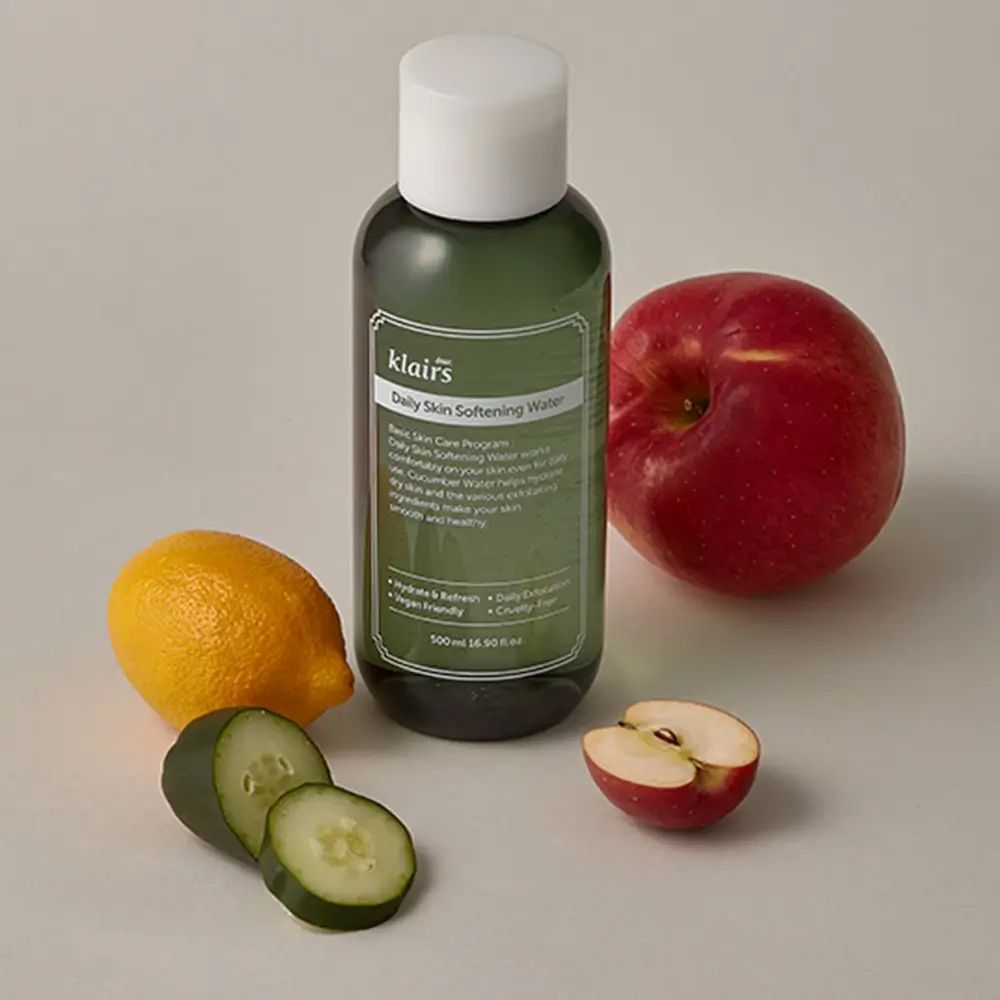 Grüne Flasche mit Produktetikett, daneben Zitrone, Apfel, Gurkenscheiben. Auf hellem Untergrund.