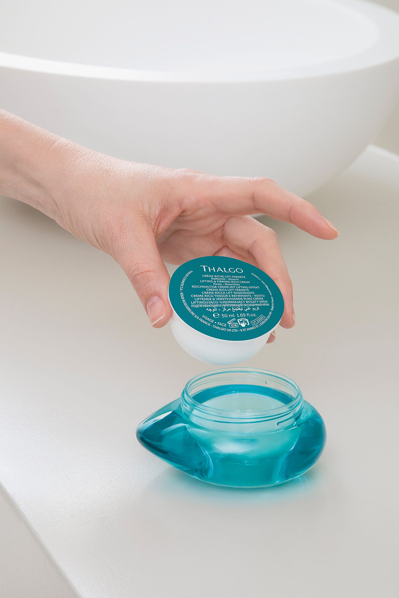 Hand hält Creme-Verpackung über leerem Glasbehälter. Aufschrift: THALGO, Crème Riche Lift-Fermeté. 50 ml.