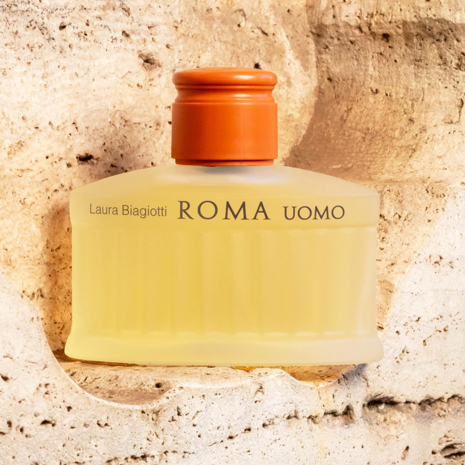 Parfümflakon mit gelblicher Flüssigkeit. Aufschrift: Laura Biagiotti ROMA UOMO. Auf Steinoptik-Hintergrund.