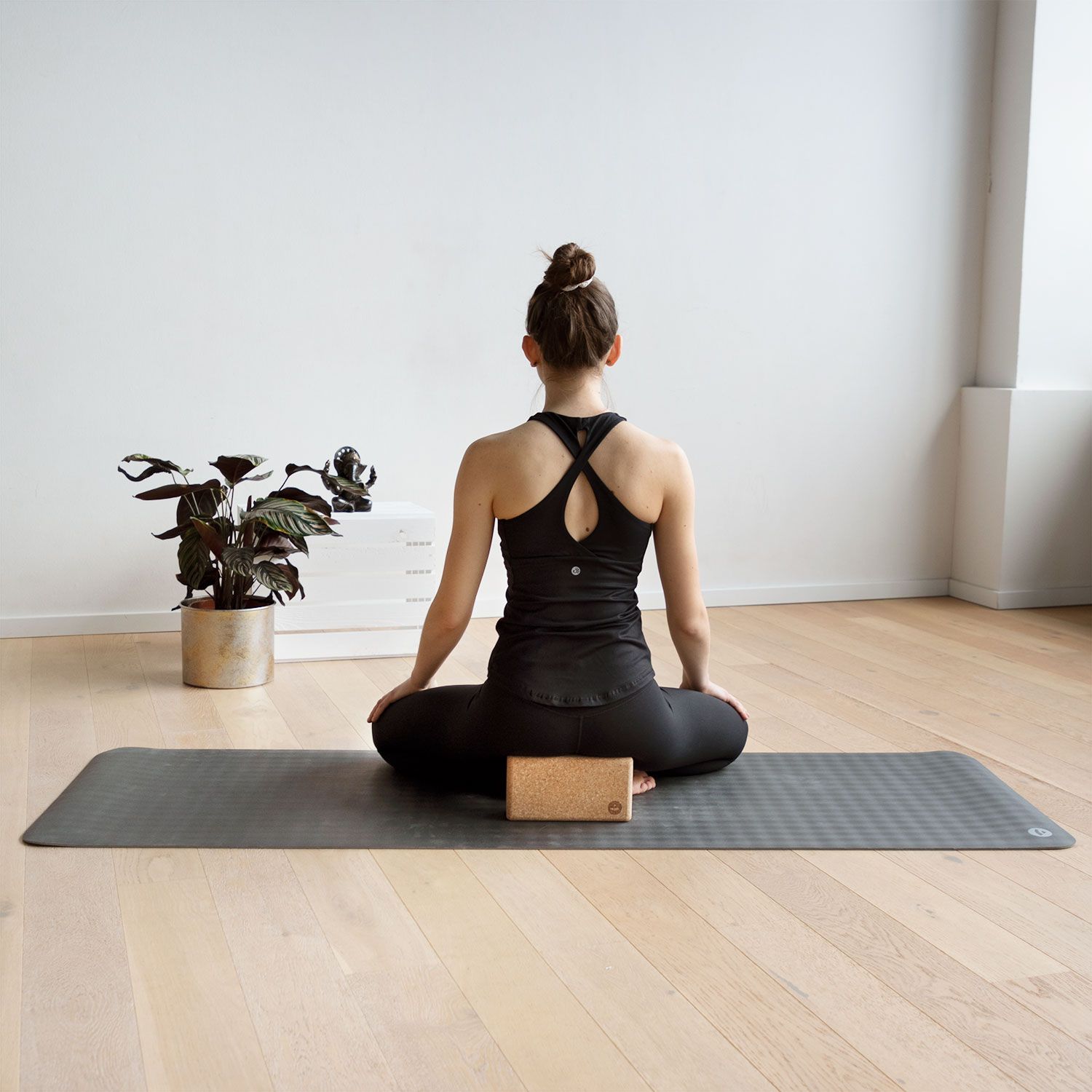 Person sitzt auf Yogamatte. Yogaklotz unter dem Gesäß. Braune Farbe. Korkmaterial.