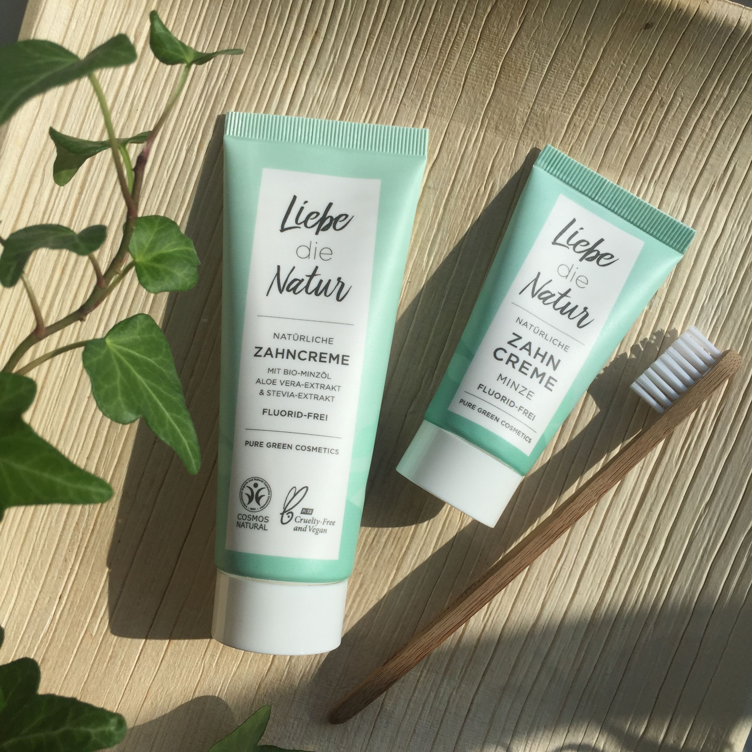 Zwei Tuben natürliche Zahncreme Minze, grüne Verpackung, neben Holzzahnbürste. Text: "Liebe die Natur".