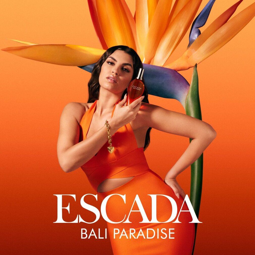 Frau hält Escada Bali Paradise EdT Nat. Spray. Frau in orangefarbener Kleidung, Produkt in der Hand.