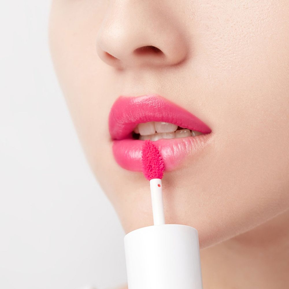 Person trägt rosa Lippenfarbe auf. Applikator wird verwendet. Nahaufnahme von Mund und Lippen.