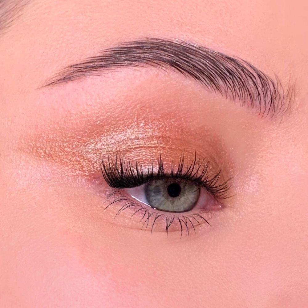 Auge mit Lidschatten. Goldfarbener Lidschatten auf dem Augenlid. Wimpern verlängert.