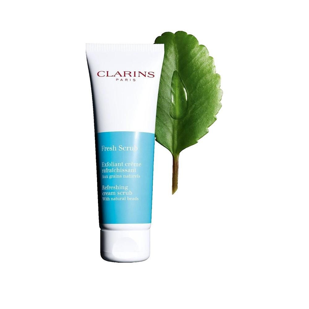 Weiße Tube mit blauem Mittelteil, Clarins Paris. Fresh Scrub. Daneben ein grünes Blatt mit Wassertropfen.