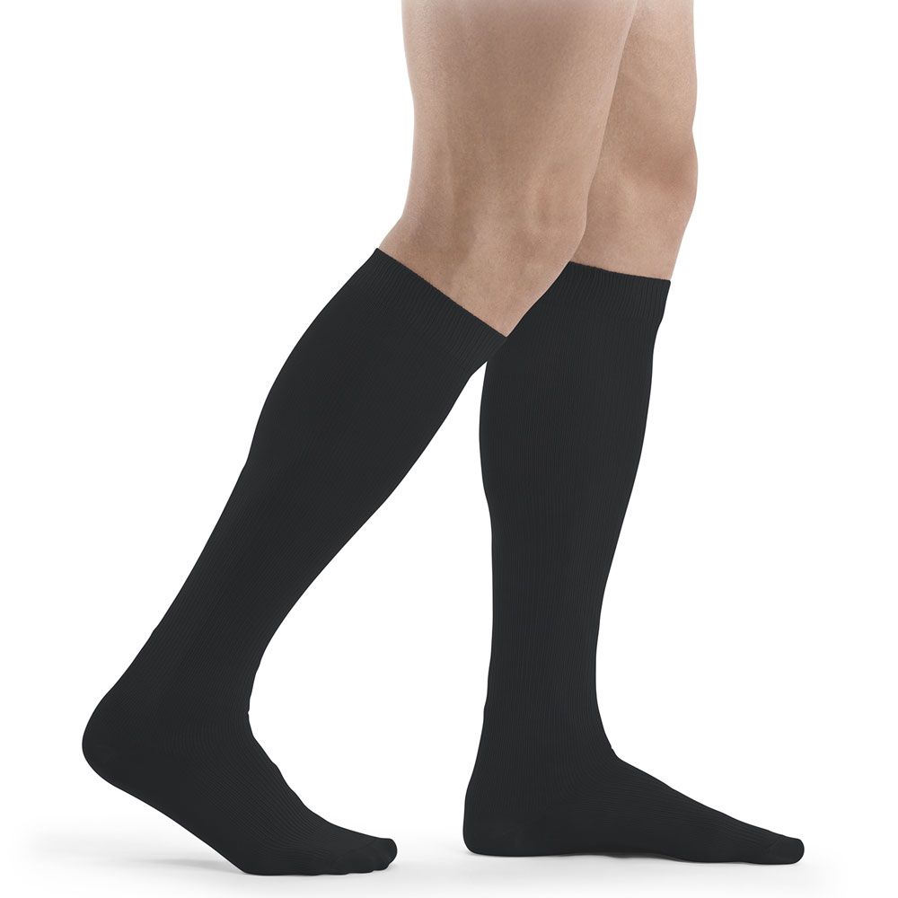 Schwarze Kniestrümpfe, vermutlich Kompressionsstrümpfe, an Beinen. Blick von der Seite, auf hellem Hintergrund.