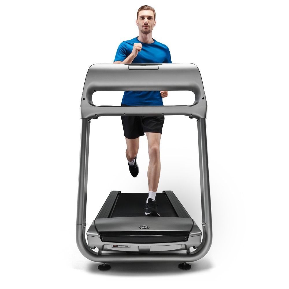 Graues Laufband mit Läufer. Sichtbare Elemente: Handläufe, Konsole, Lauffläche. Der Mann trägt Sportkleidung.