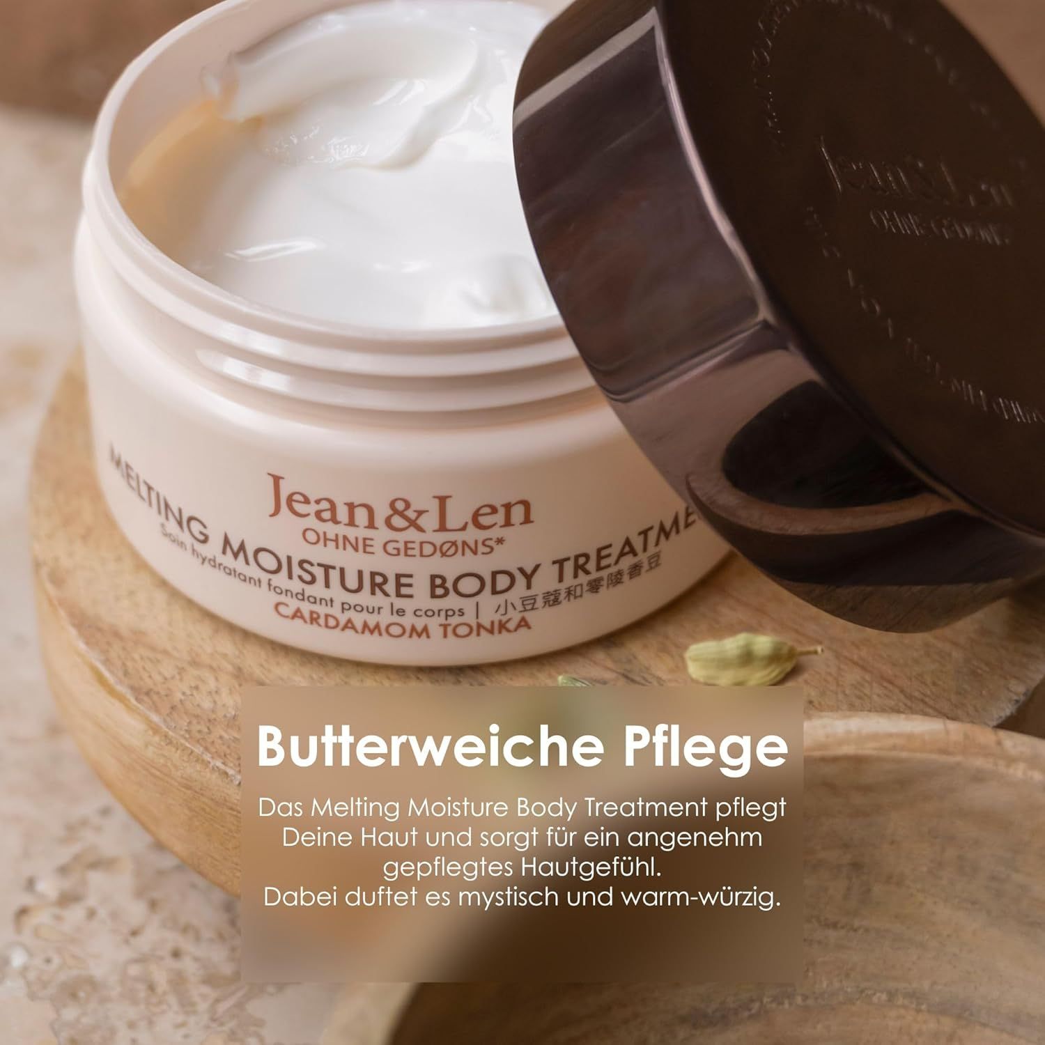 Geöffneter Cremebehälter mit weißer Creme. Deckel daneben. Aufschrift: Melting Moisture Body Treatment Cardamom Tonka.
