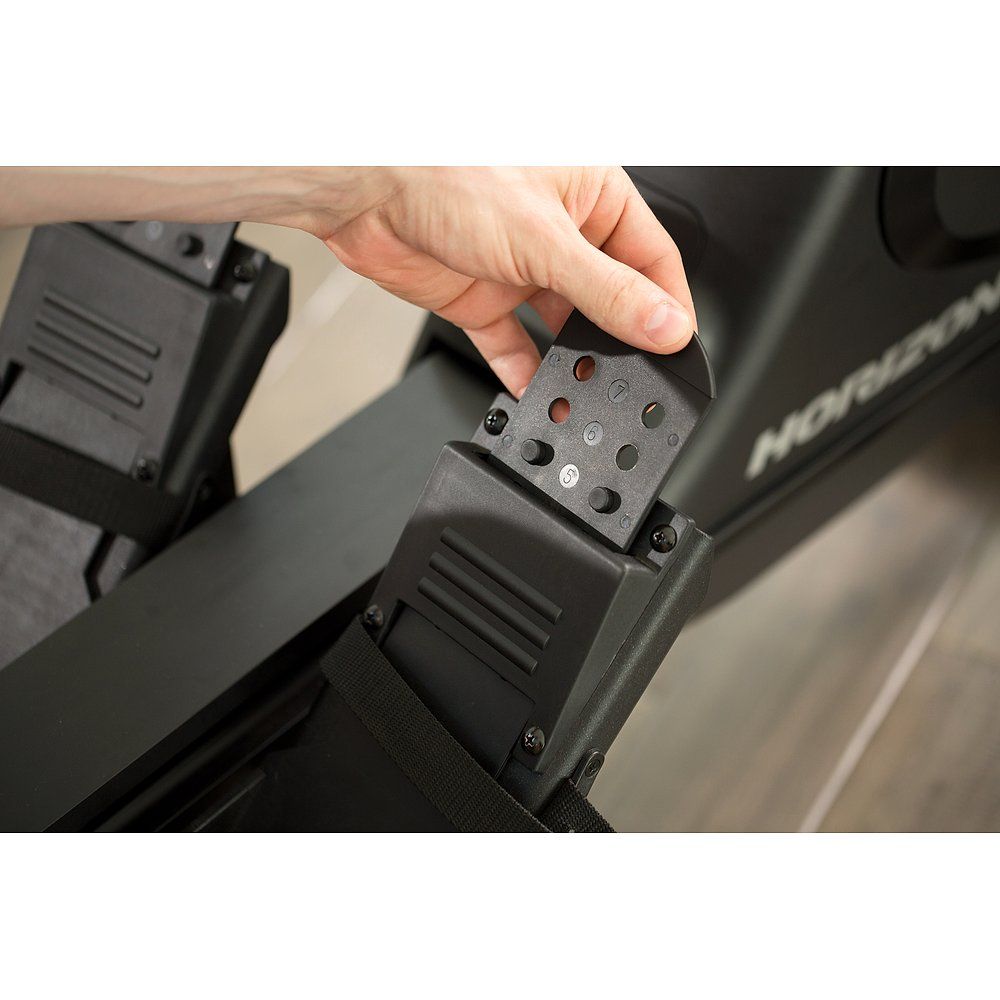 Nahaufnahme von Teilen des Rudergeräts. Schwarze Kunststoffteile mit Schrauben und Löchern. Hand hält Teil.