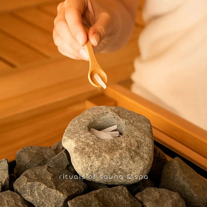 Hand hält Holzlöffel mit Kristallen über Stein mit Kristallen. Aufschrift: rituals of sauna & spa.