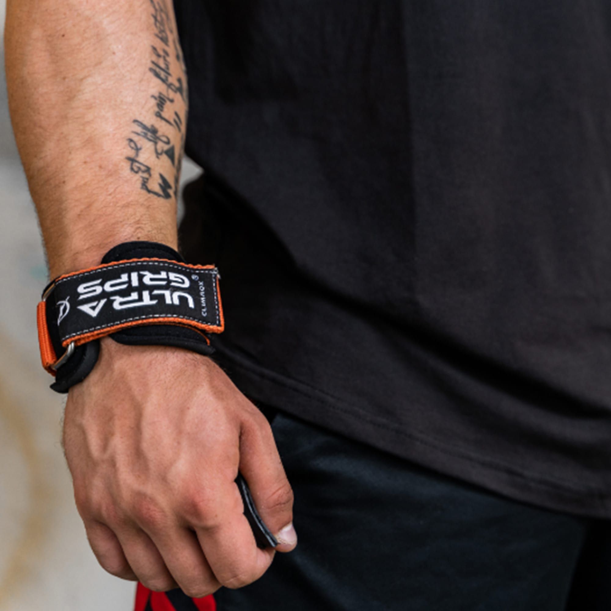 Nahaufnahme eines Handgelenks mit einem Ultra Grip. Schwarzes Band mit orangefarbenen Akzenten und "ULTRA GRIPS".