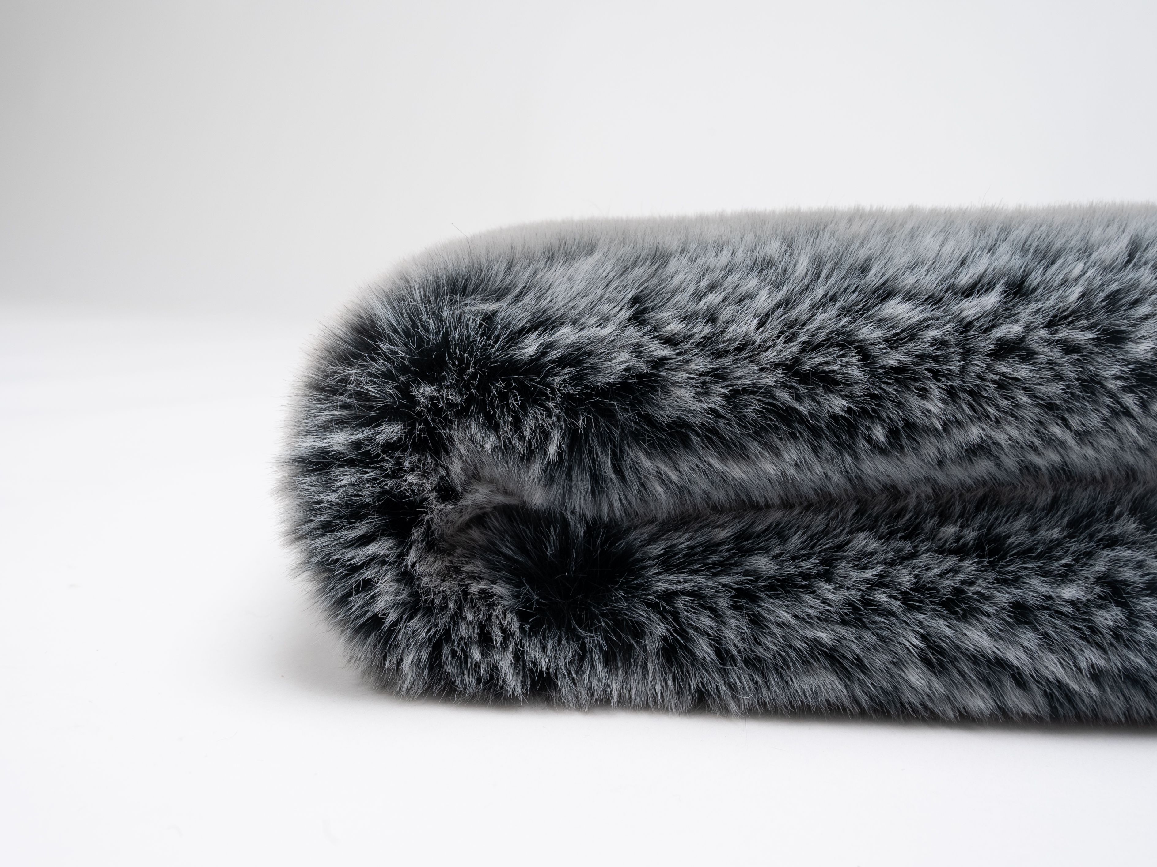 Gerollte graue Hundedecke. Weiches, flauschiges Material. Auf weißem Hintergrund.