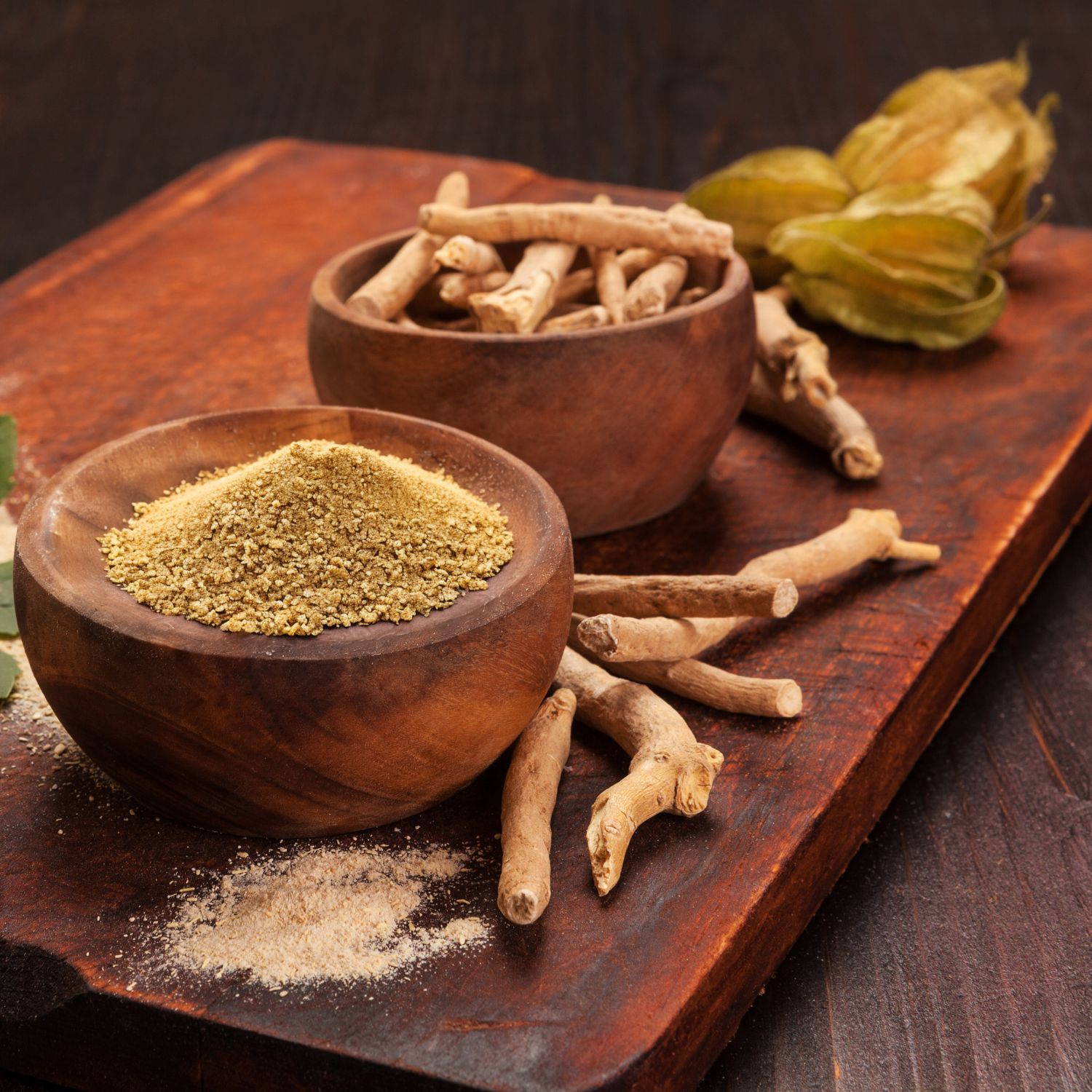 Holzbrett mit zwei Holzschalen. Eine Schale mit Pulver, die andere mit Stäben. Ashwagandha-Pflanze.