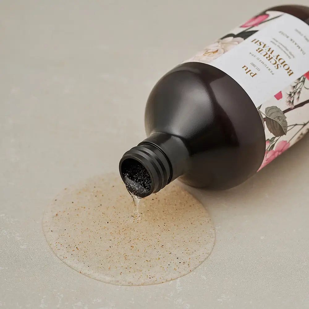 PLU Scrub Body Wash Damask Rose wird aus einer braunen Flasche auf eine Oberfläche gegossen.