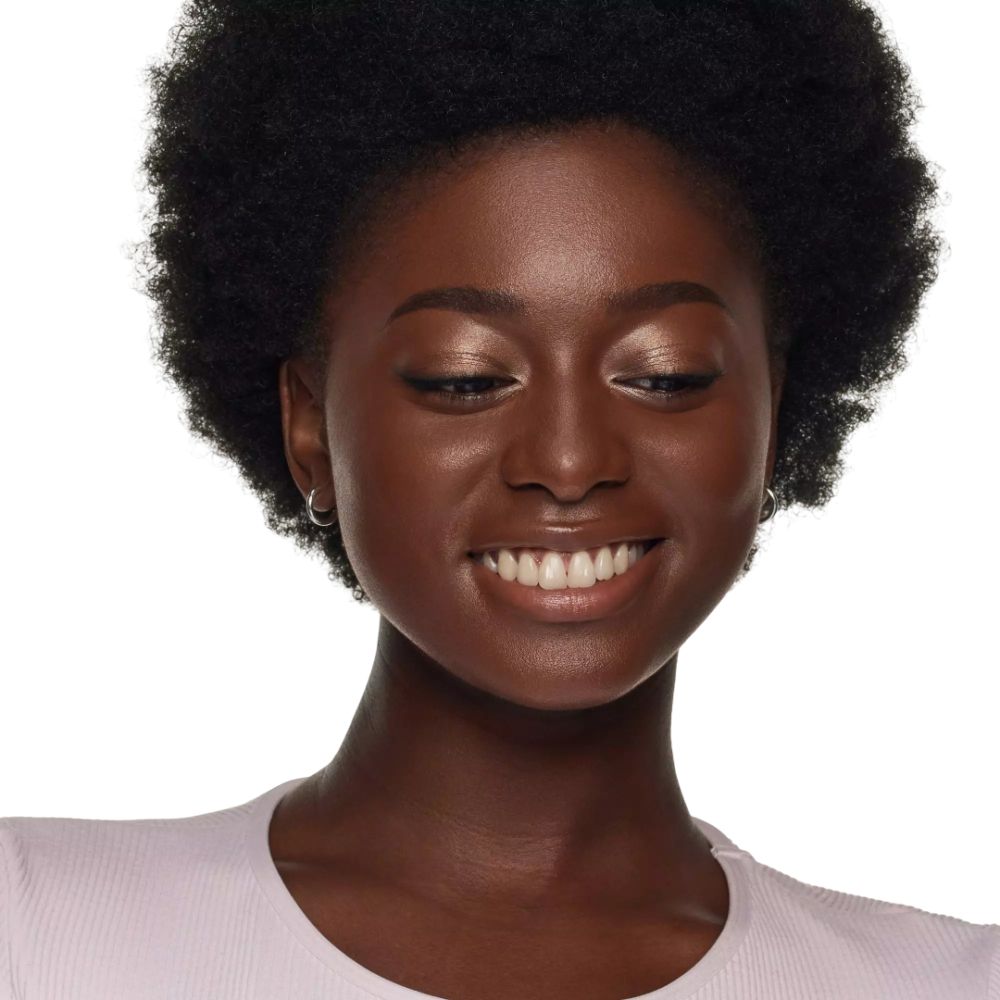 Porträt einer lächelnden Frau mit dunkler Haut. Sie trägt hellen Lidschatten und Ohrringe.