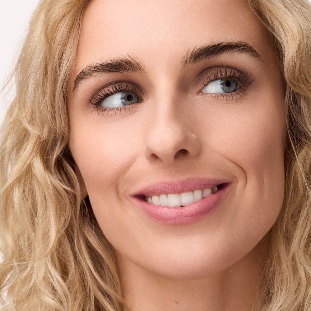 Porträt einer Frau mit blonden Locken, die zur Seite schaut und lächelt. Rosa Lippenstift.