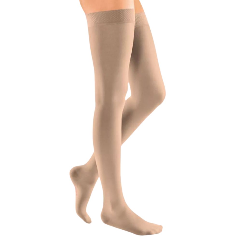 Beige Kompressionsstrümpfe, kniehoch, mit Spitze am oberen Rand. Die Strümpfe bedecken die Füße und Beine.