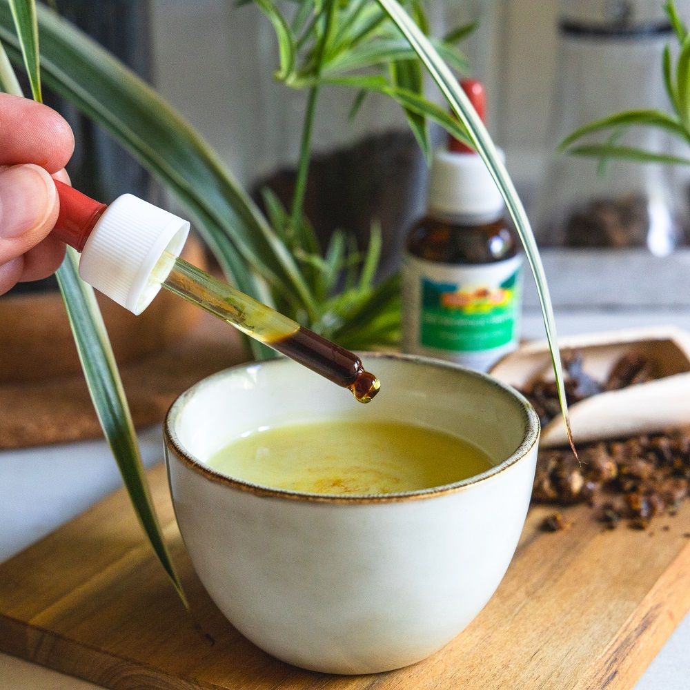 Hand hält Tropfer über Schale mit Flüssigkeit. Daneben Holzbrett mit Propolis und Flasche.