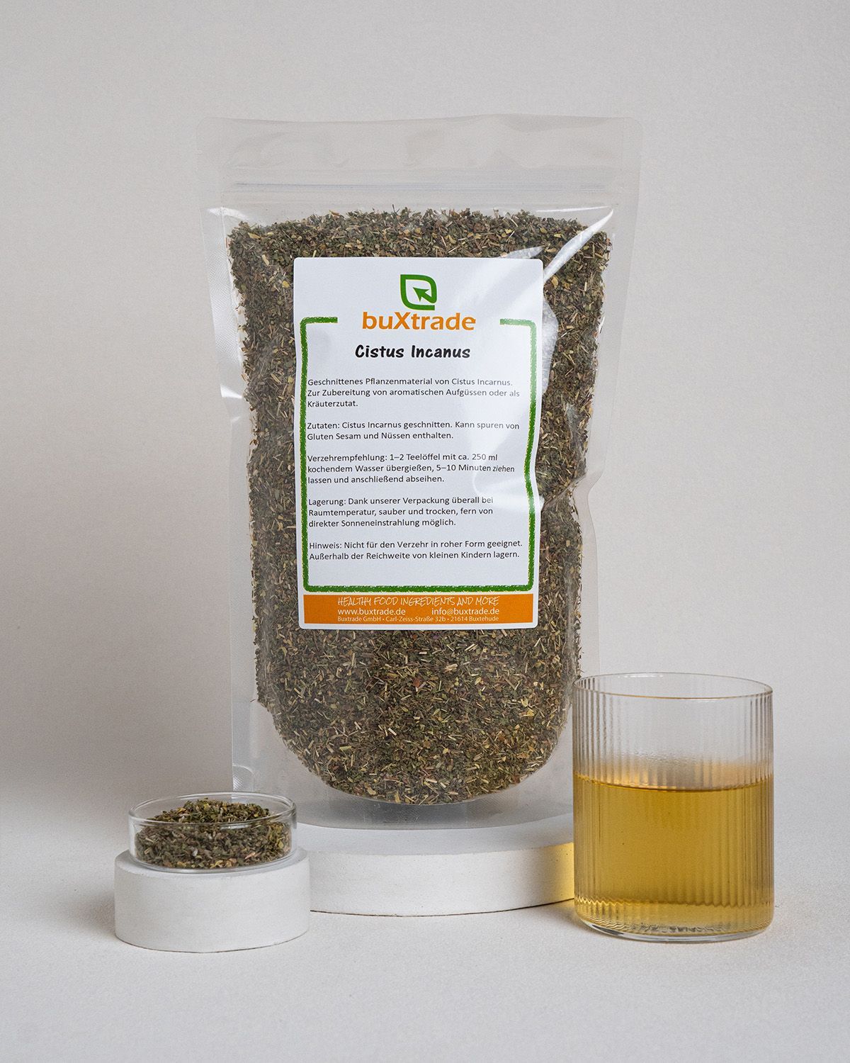 Produktpräsentation mit Kräutern, Glas und Flüssigkeit. buXtrade Cistus Incanus. Transparente Verpackung, Glas.