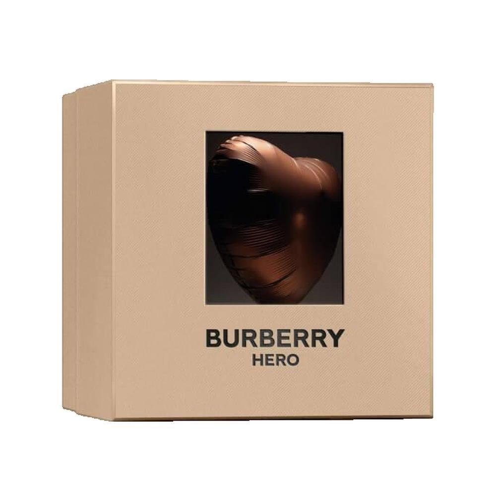 Beige Verpackung mit quadratischem Fenster. Durch das Fenster ist eine bronzefarbene Skulptur in Herzform zu sehen. "Burberry Hero" steht darunter.