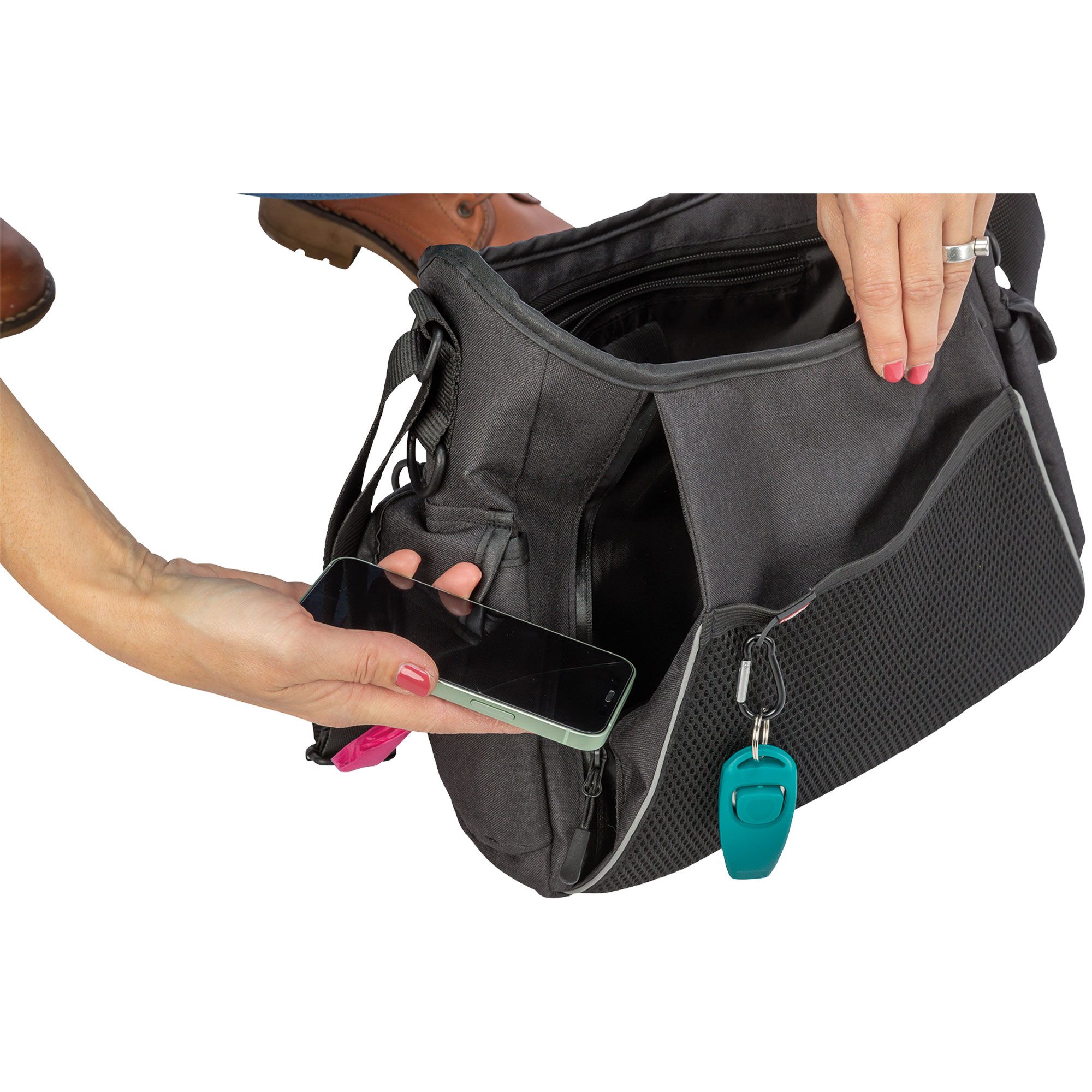 Graue Umhängetasche, geöffnet. Eine Hand legt ein Smartphone hinein. Schlüsselanhänger mit Schlüssel.